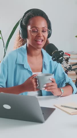 A cheerful individual engages in lively dialogue while holding a cup, surrounded by a vibrant studio filled with plants and creative materials, creating an inviting atmosphere.