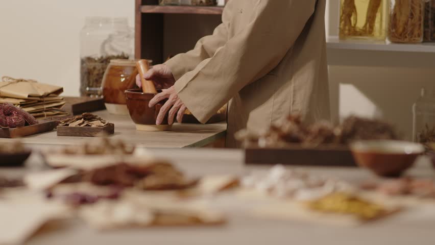 A traditional oriental medicine room features a herbalist grinding herbs with a wooden pestle in a brown stone mortar, serving as a template video for traditional medicine content.