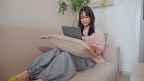 Asian young teenager woman using digital tablet in living room at home. Adorable girl sitting on sofa and smiling while holding tablet for virtual distancing studying online learning alone in house  - Powered by Shutterstock - Get 15% off with code: PIKWIZARD15