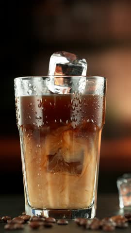 Super Slow Motion of Falling Ice Cube Into Coffee Drink, Close-up, Camera in Motion. Filmed on High Speed Cinema Camera, 1000 fps. Vertical Composition.