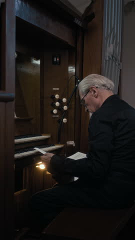 Vertical shot of elderly organist placing sheet music on stand while sitting at organ and preparing for rehearsal