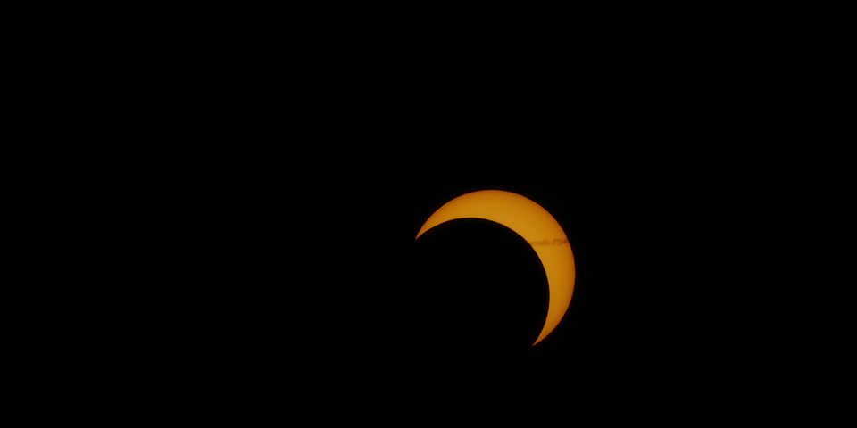 Solar eclipse with the remains of a jet’s contrail during the event’s partial phase of 75% coverage. October 14, 2023.