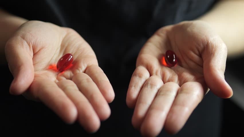 Caucasian hands opening to reveal red capsules pills tablets.