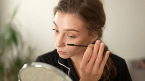 Beautiful woman applying mascara to her eyes looking in small mirror. Cute woman applying makeup sitting in bright room. Makeup, beauty, naturalness concept. - Powered by Shutterstock - Get 15% off with code: PIKWIZARD15