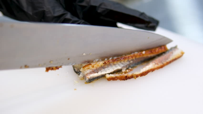 cut the eel a chef in black gloves cuts pieces of eel fish for sushi with a large knife