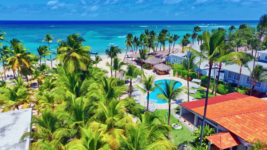 Aerial view of tropical resort palm beach on Caribbean coast. Blue ocean waters view from above. Beautiful Atlantic hotel beach with palm trees and swimming pool. Relaxation on the sea.