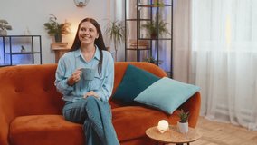 Pretty smiling happy Caucasian young woman drinking a cup of warm coffee or herbal tea sitting on home orange couch in the morning. Girl enjoying comfortable relaxing alone at living room apartment - Powered by Shutterstock - Get 15% off with code: PIKWIZARD15