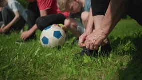 Close-up of four people in an outdoor setting, with three kneeling down to tie their shoelaces while a little boy places his hand on a soccer ball - Powered by Shutterstock - Get 15% off with code: PIKWIZARD15