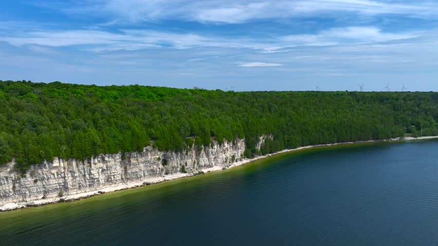 Aerial drone footage of Fayette Park and striking limestone cliffs in Fayette, Michigan on a beautiful and warm Summer day in July. Blue sky and wind turbines above calm Lake Michigan