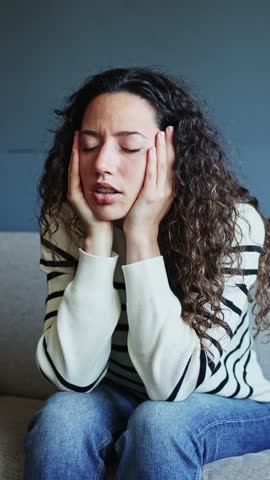 Young woman sitting on a sofa, feeling emotional pain and anxiety while grappling with overwhelming thoughts and worries. Young woman suffering from anxiety at home
