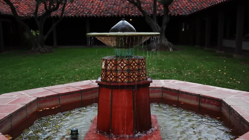 Water Fountain In Green Grass Courtyard With Red Tile Roof And Trees
