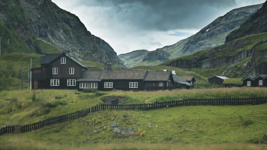 Traditional wooden buildings sit in a green Boverdalen valley, surrounded by towering mountains and rocky slopes.