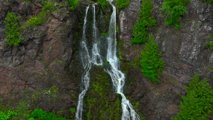 Aerial drone footage of Douglass Houghton Waterfall in Michigan on a beautiful and cool Summer day in July. Scenic waterfall cascading down rocky cliffs in lush green forest