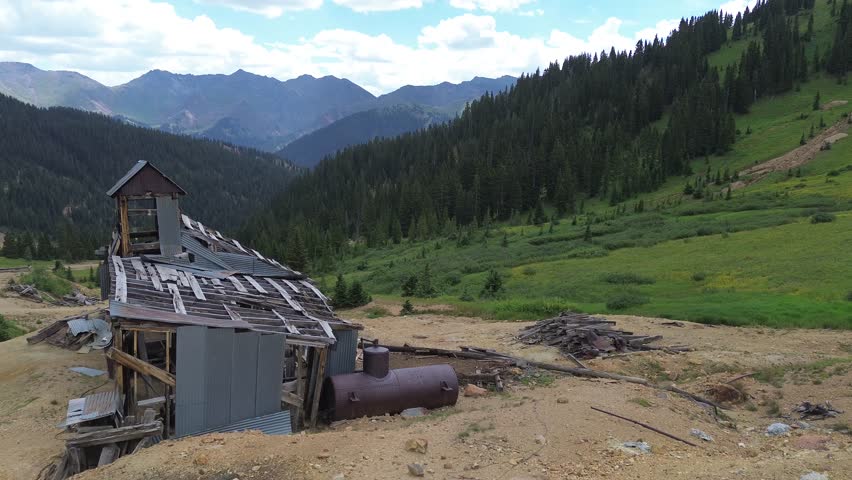 Aerial flyover shot of an abandoned, very decayed mine in the San Juan Mountains near Silverton Colorado. Flight goes over the structure to show the mountain scenery surrounding the site.