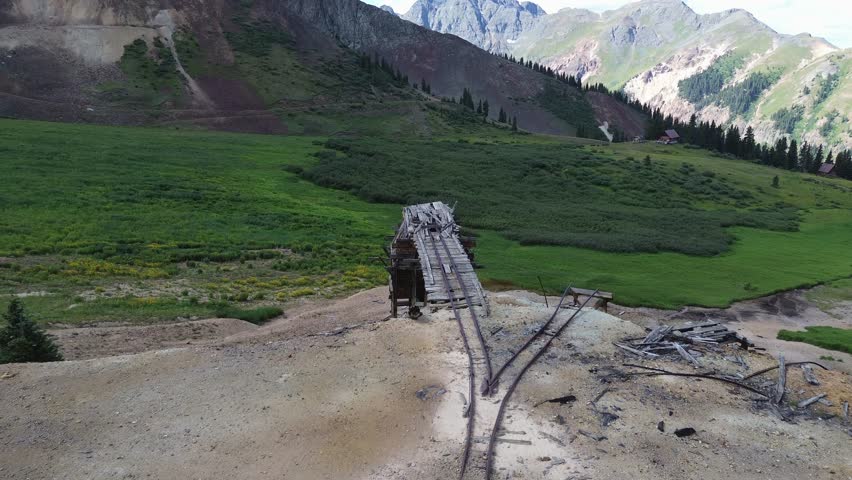 Abandoned mine ruins in the San Juan Mountains of Colorado. Very decayed structure surrounded by mountain scenery and alpine cabins. Flight is along the old ore cart rails on top of the structure.