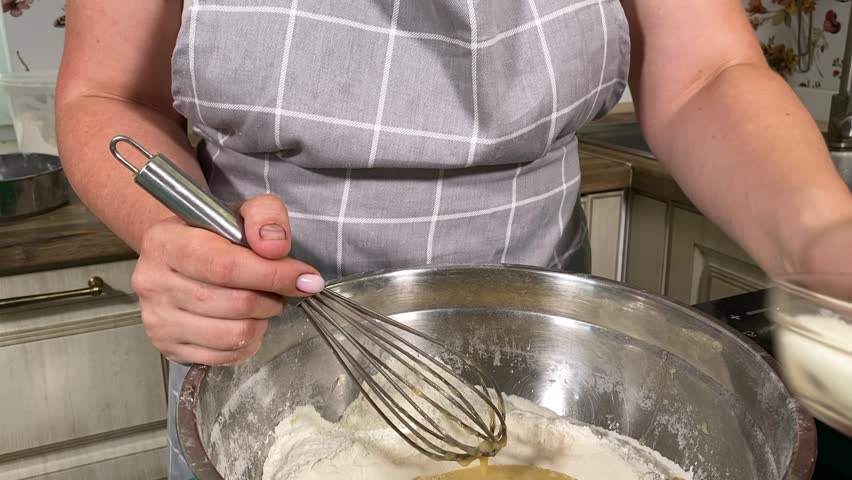 A young attractive housewife preparing yeast dough in home kitchen. Woman mixes ingredients, working the dough with precision to create a perfect base. Traditional baking and homemade culinary skills