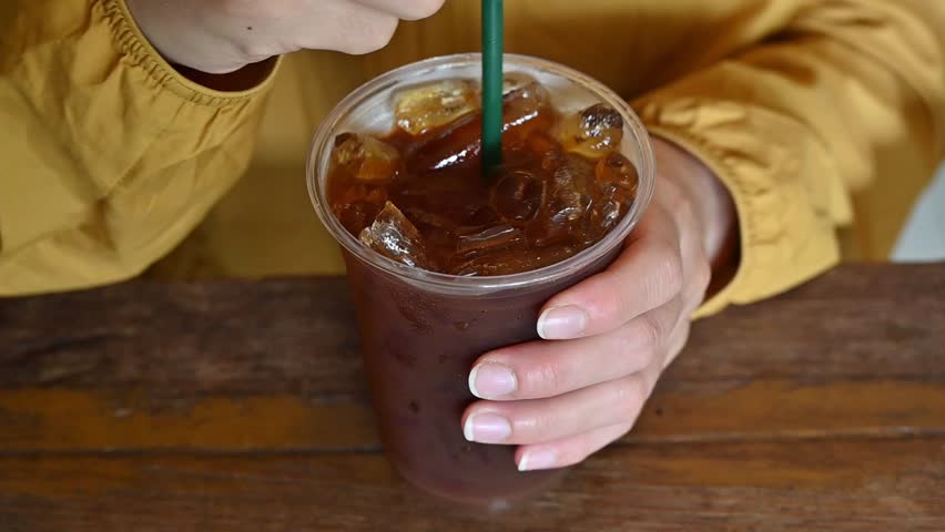 Footage of woman stirring an iced Americano coffee before drinking. The Iced Americano is a simple classic made with espresso, water and ice.