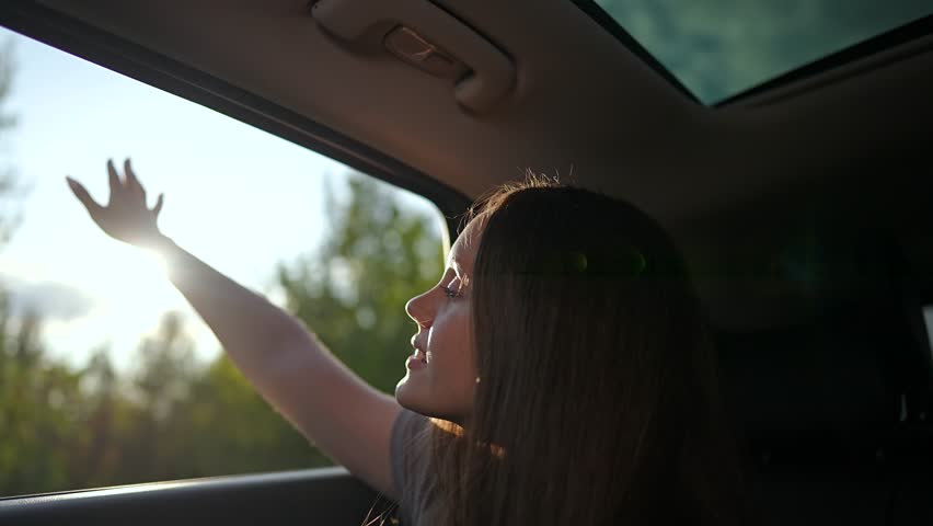 Happy woman enjoys trip with hand out window. Sunlight shines as she feels breeze through open window. Carefree woman embraces freedom on road trip. Joyful travel moment. Window down, happy trip vibes