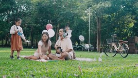 Happy Asian family having a picnic in the park, with dad playing guitar while others play with soap bubbles. - Powered by Shutterstock - Get 15% off with code: PIKWIZARD15