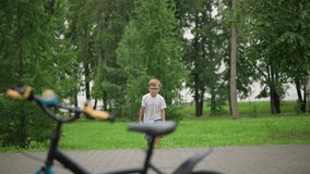 A young boy, wearing glasses, jumps joyfully toward a parked bicycle with a determined look and a stern smile on his face, dressed in a white top and denim shorts - Powered by Shutterstock - Get 15% off with code: PIKWIZARD15