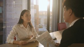 Business professionals discuss contract details sitting at table at sunset light. Asian HR manager interviews vacancy candidate in modern workspace. Commercial agreement - Powered by Shutterstock - Get 15% off with code: PIKWIZARD15