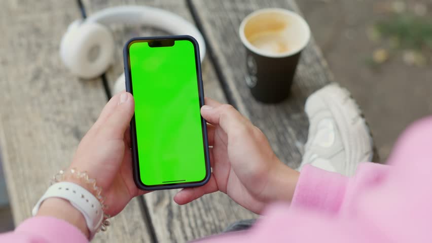 Young Woman Using Smartphone in Vertical Mode with Green Mock-up Screen Outside, Doing Swiping, Scrolling Gestures. Internet Social Networks Browsing News, Financial Reports - Powered by Shutterstock - Get 15% off with code: PIKWIZARD15