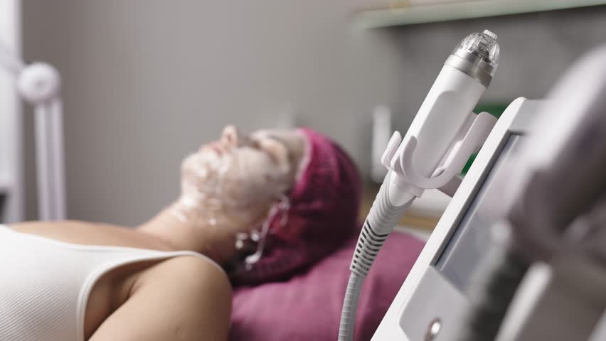 A young woman in a modern cosmetology salon waits for the anesthesia to take effect before the microneedle RF lifting procedure. This shot emphasizes the careful preparation for the treatment.