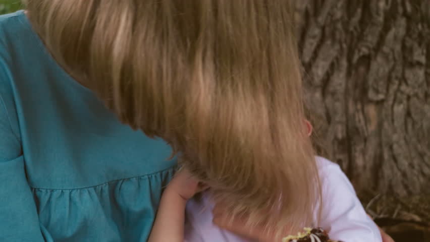 A mother and her child, with their faces affectionately close and both laughing, the mother holds a cake while the child touch his nose
