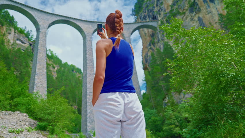A girl takes a selfie in front of the world famous Landwasser Viaduct in Switzerland in the summer