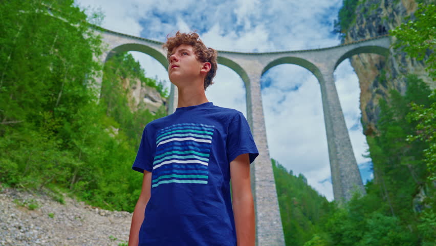 A teenage boy stands in front of the world famous Landwasser Viaduct in Switzerland in the summer