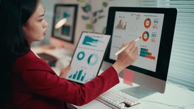 Businesswoman in red suit is sitting at her desk and analyzing financial data on a computer screen. She is holding a pen and pointing at the screen - Powered by Shutterstock - Get 15% off with code: PIKWIZARD15