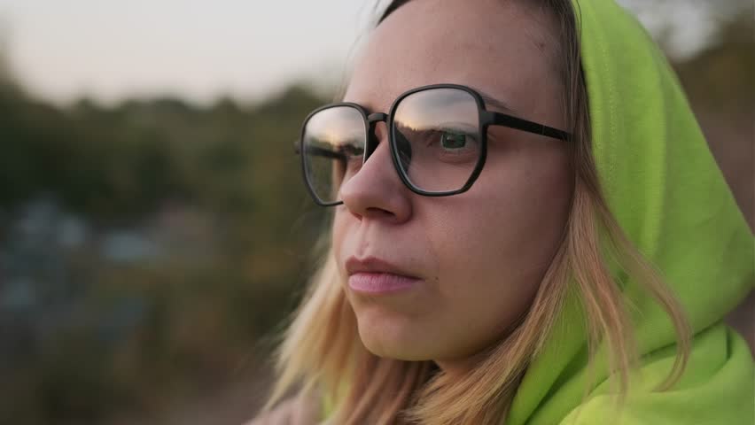 Woman in a vibrant green outfit sitting thoughtfully on a hillside during sunset, enjoying nature in a serene environment