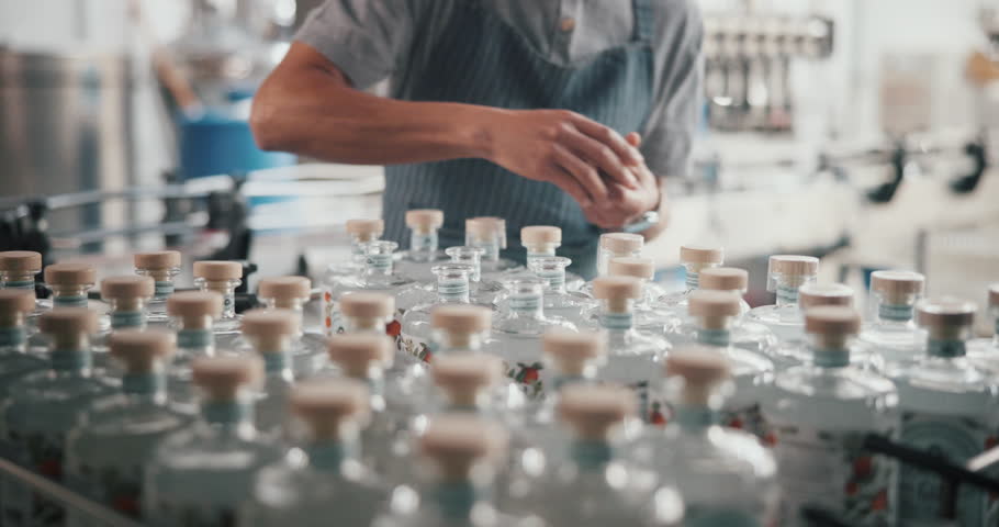 Hands, man and packaging alcohol at distillery with gin bottles for manufacturing and production at warehouse. Male person, business and employee with stocktaking at factory for delivery and supply