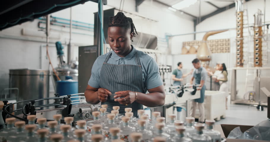 Happy, black man and packaging alcohol at distillery with gin bottles for manufacturing and production at warehouse. Male person, employee and stocktaking at factory for delivery and supply chain