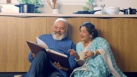 Joyful Indian Asian senior couple sitting comfortably on the kitchen floor, relaxing with cups of tea,fondly looking through an old photo album, reliving cherished memories together - Powered by Shutterstock - Get 15% off with code: PIKWIZARD15