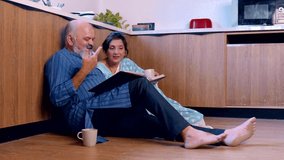 Joyful Indian Asian senior couple relaxing on the kitchen floor sipping tea together, looking through an old photo album and the husband fondly rewinding memories sharing with his wife - Powered by Shutterstock - Get 15% off with code: PIKWIZARD15