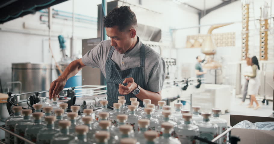 Business, man and packaging alcohol at distillery with gin bottles for manufacturing and production at warehouse. Male person, employee and serious with stocktaking at factory for delivery and supply