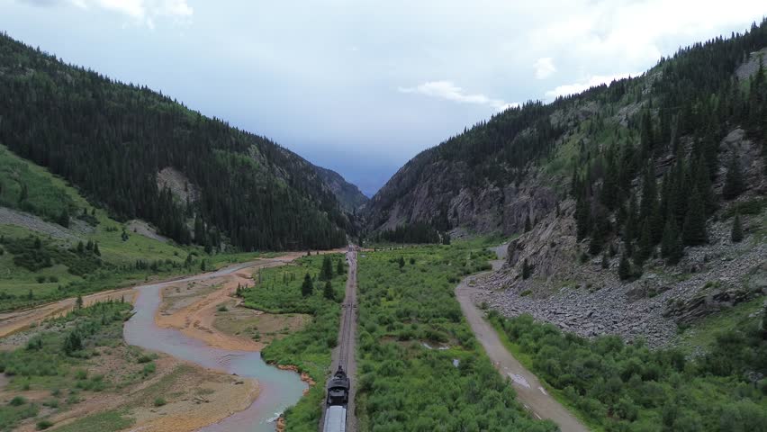 Scenic narrow gauge passenger train pulled by a steam engine leaves  the Silverton, Colorado area. In the background are scenic mountains and the Animas River.