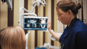 Professional female stomatologist discussing with patient in dental clinic. Middle-aged oral surgeon and young client of modern dental clinic viewing cat scans on display, plan of dental treatments - Powered by Shutterstock - Get 15% off with code: PIKWIZARD15