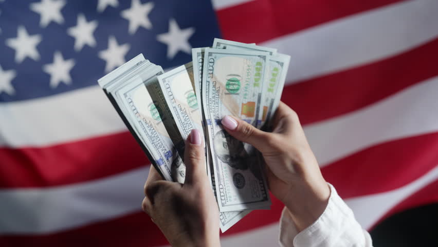 Counting money dollars USD on waving american national flag background. Finance, economic crisis, united states currency, symbol of independence.