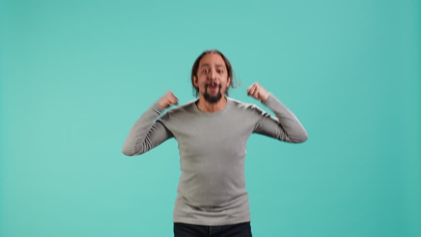 Man jumping from joy in excitement while cheering for favorite sports team, studio background. Person celebrating after victory, showing intense enthusiasm, supporting team during game, camera A