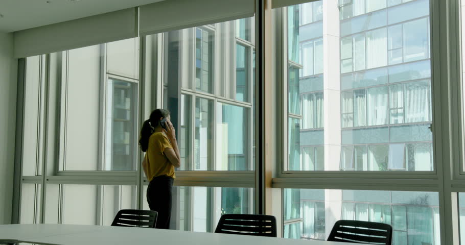Businesswoman on a Phone Call in an Empty Office Conference room Looking out of the window
