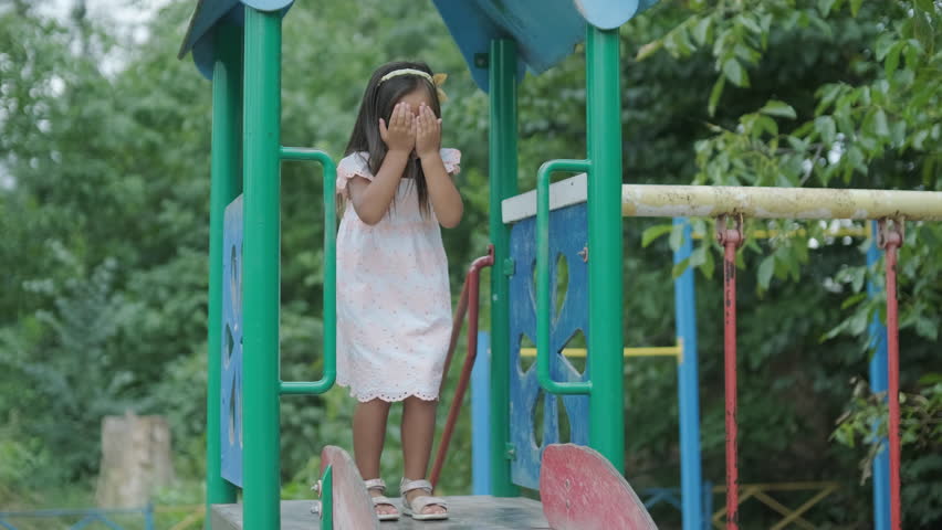 A pregnant mother and her young daughter enjoy playful time together at a playground in the park, surrounded by trees and greenery