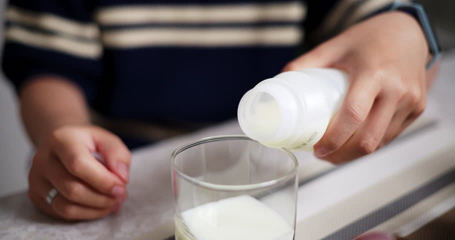 Handheld selective focus shot, Young Asian woman pouring milk into a drinking glass while eating lunch on table at home. Lifestyle at home