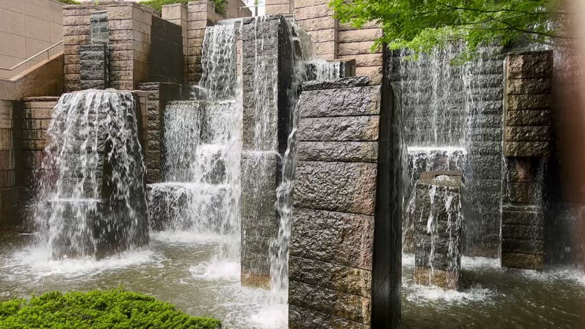 Waterfall, the waterfalls at the Gotenyama Garden in Shinagawa in a park at daytime at the end of summer in Tokyo city. Down falling water from a waterfall with green leaves of Japanese maple tree.