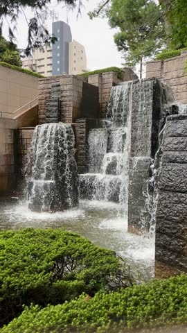 Waterfall, vertical video of the waterfalls in Gotenyama Garden in Shinagawa city at daytime in summer in Tokyo Japan. Down falling water from a waterfall with green leaves of Japanese maple tree.