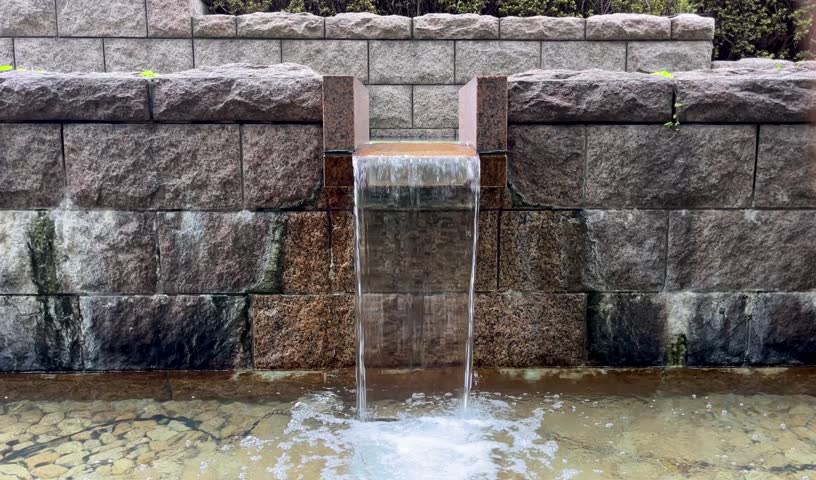 Waterfalls, water falling down from a waterfall outside in the Gotenyama Garden in Shinagawa at daytime in Tokyo Japan. A wall from stone with a small water stream with space for text. 