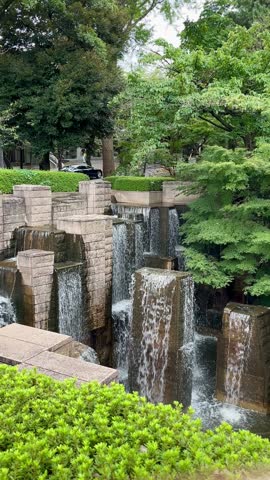 Waterfall, vertical video of the waterfalls in Gotenyama Garden in Shinagawa outdoor at daytime between the green trees in summer in Tokyo city in Japan.