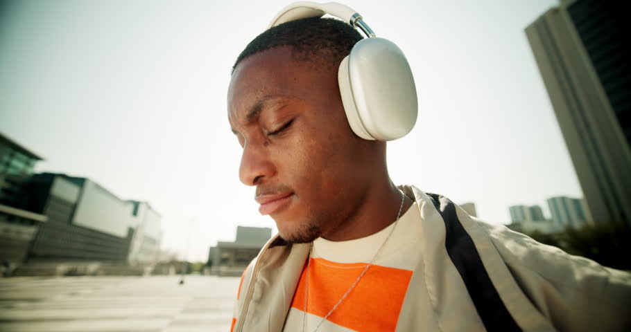 Fashion, walking and black man with headphones, outdoor and listening to music with urban town. African person, lens flare and guy with headset, song and sound with stylish clothes, trendy outfit