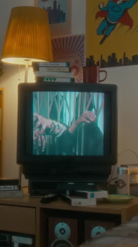 No people vertical shot of 90s retro bedroom decorated with bright posters, old tube tv with horror movie on screen